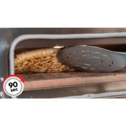 Pizza crust browning inside a toaster oven with a slotted spatula resting on the rack and a 90-second timer sticker on the oven door.